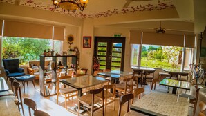 Un vaste espace dédié à la salle à manger, avec de nombreuses tables et chaises, de grandes fenêtres offrant une vue sur l’extérieur, des ventilateurs de plafond et un lustre.
