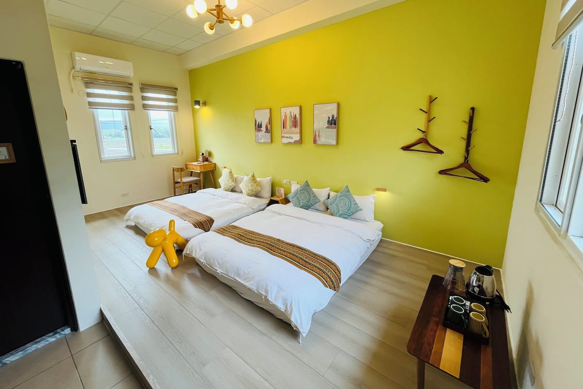 A hotel room with two beds, a desk, a chair, a small table with a tray, and a window.