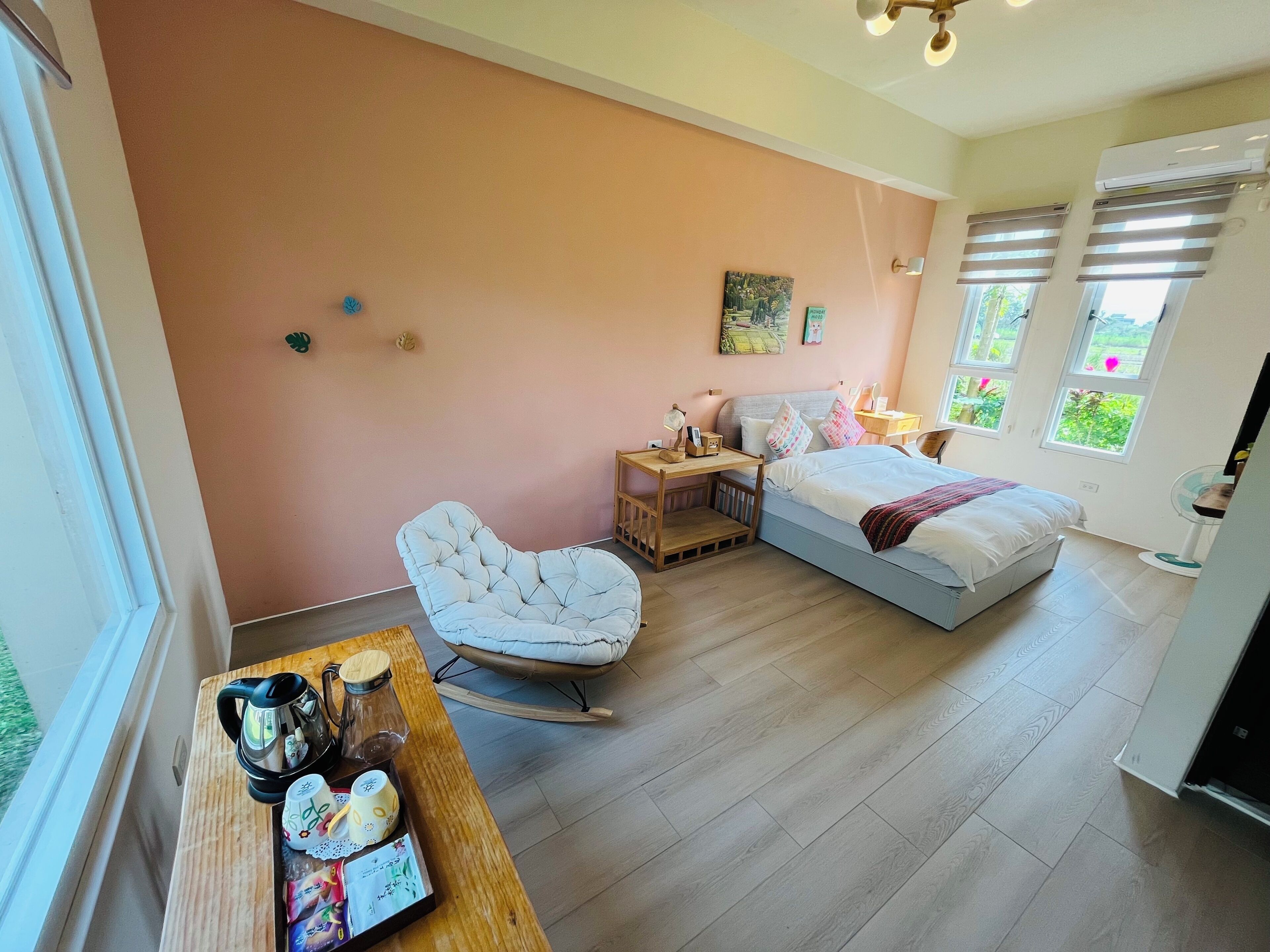 Ein Schlafzimmer mit einem Bett, einem Sessel, einem Tisch mit Wasserkocher und Tassen sowie einem Fenster mit Jalousien.