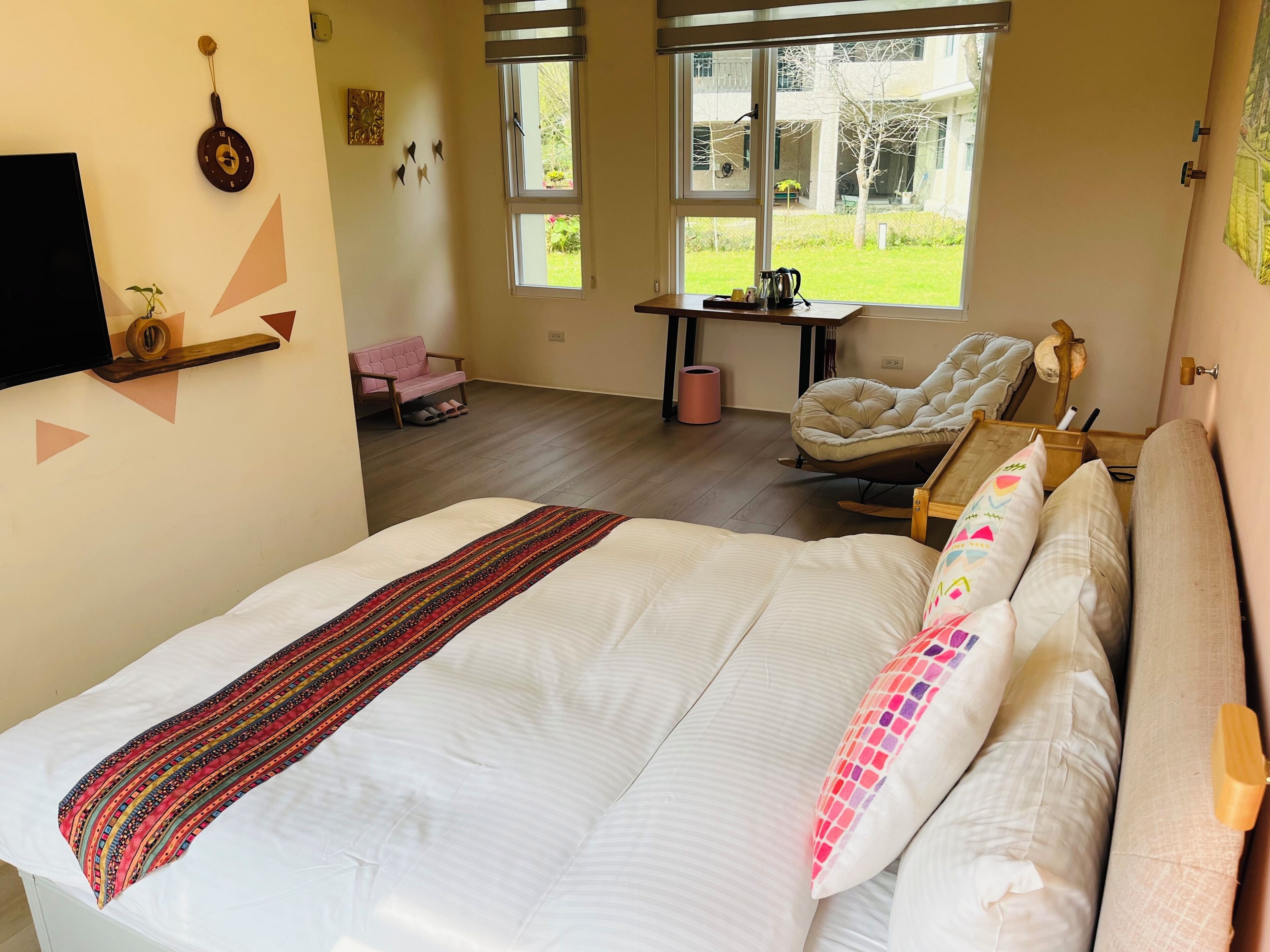 A bedroom with a large bed, a chair, a small table, and a window with a view of the outdoors.