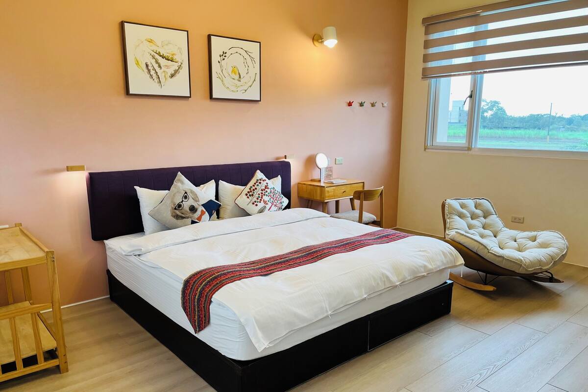 A bedroom with a bed, a chair, a nightstand, and wall art.