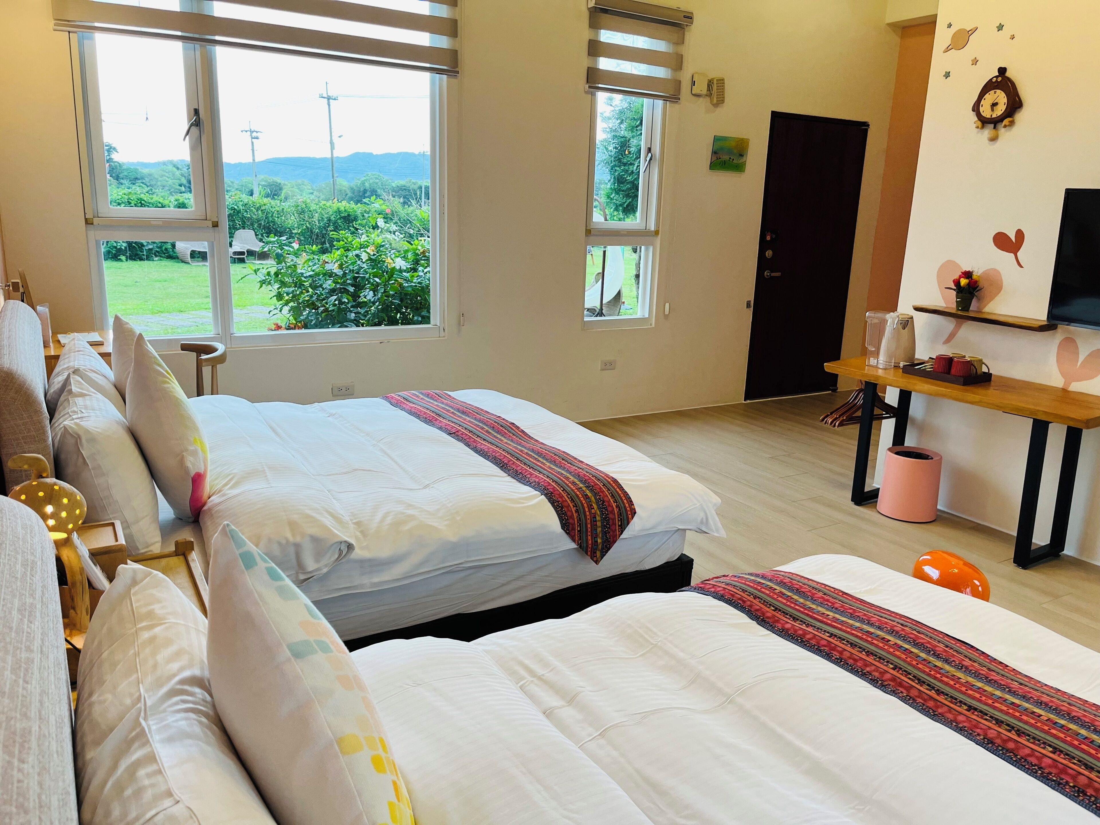 Quarto de hotel com duas camas, uma escrivaninha de madeira, televisão e vista para o verde lá fora.