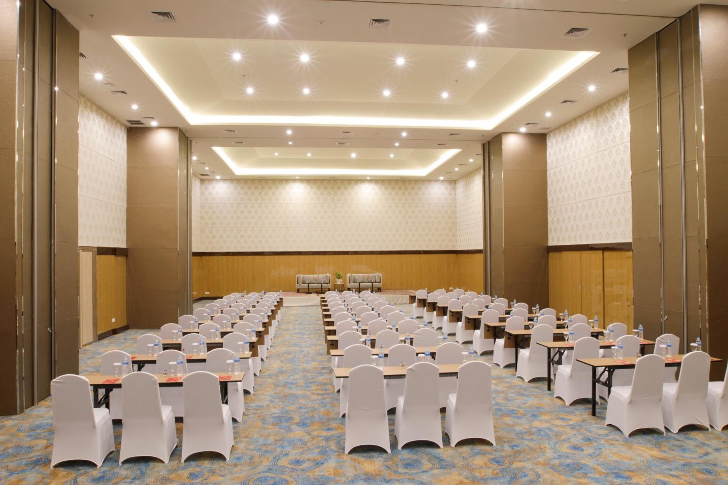 A conference room with rows of tables and chairs, a patterned carpet, and a ceiling with recessed lighting.