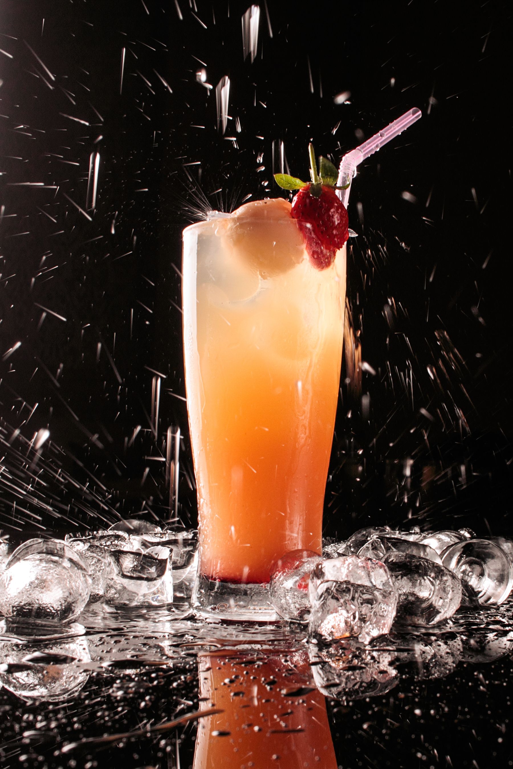 Un vaso alto con fresas y una pajita, rodeado de cubitos de hielo.