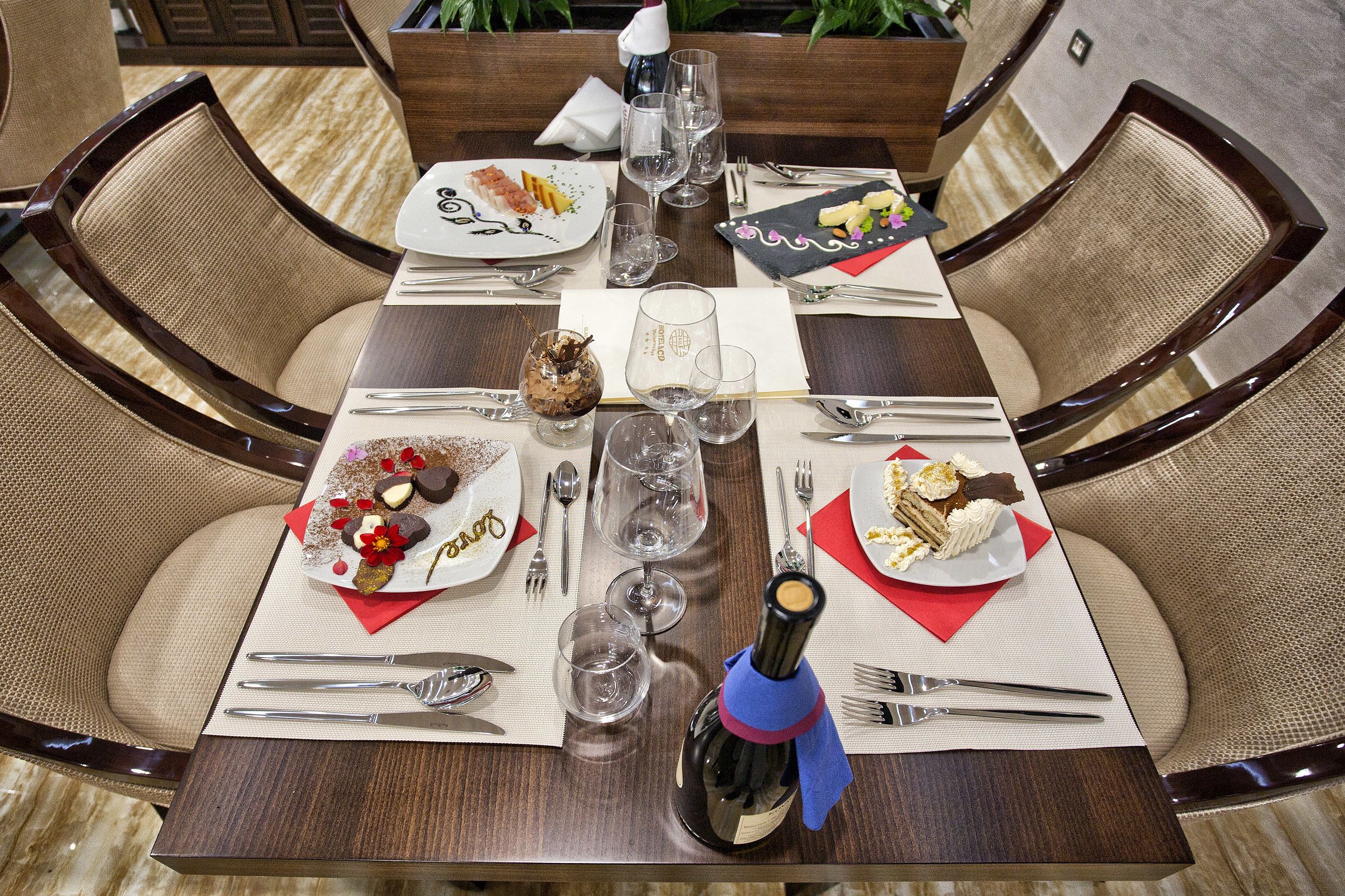 Mesa de jantar posta para quatro com taças de vinho, pratos de comida e talheres.