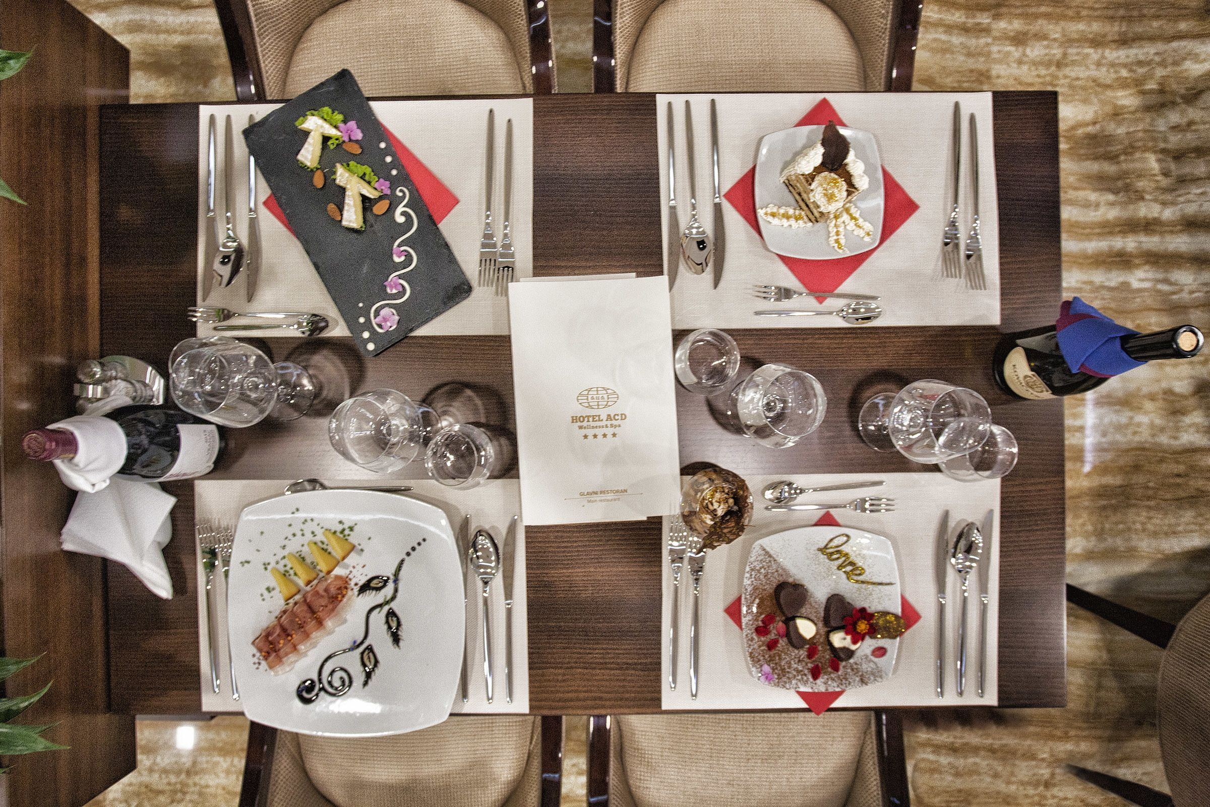 A dining table set with plates, cutlery, glasses, and a bottle of champagne.