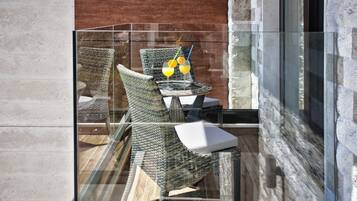 A glass-enclosed balcony with wicker chairs and a small table, featuring a glass of orange juice and a cocktail with a straw.