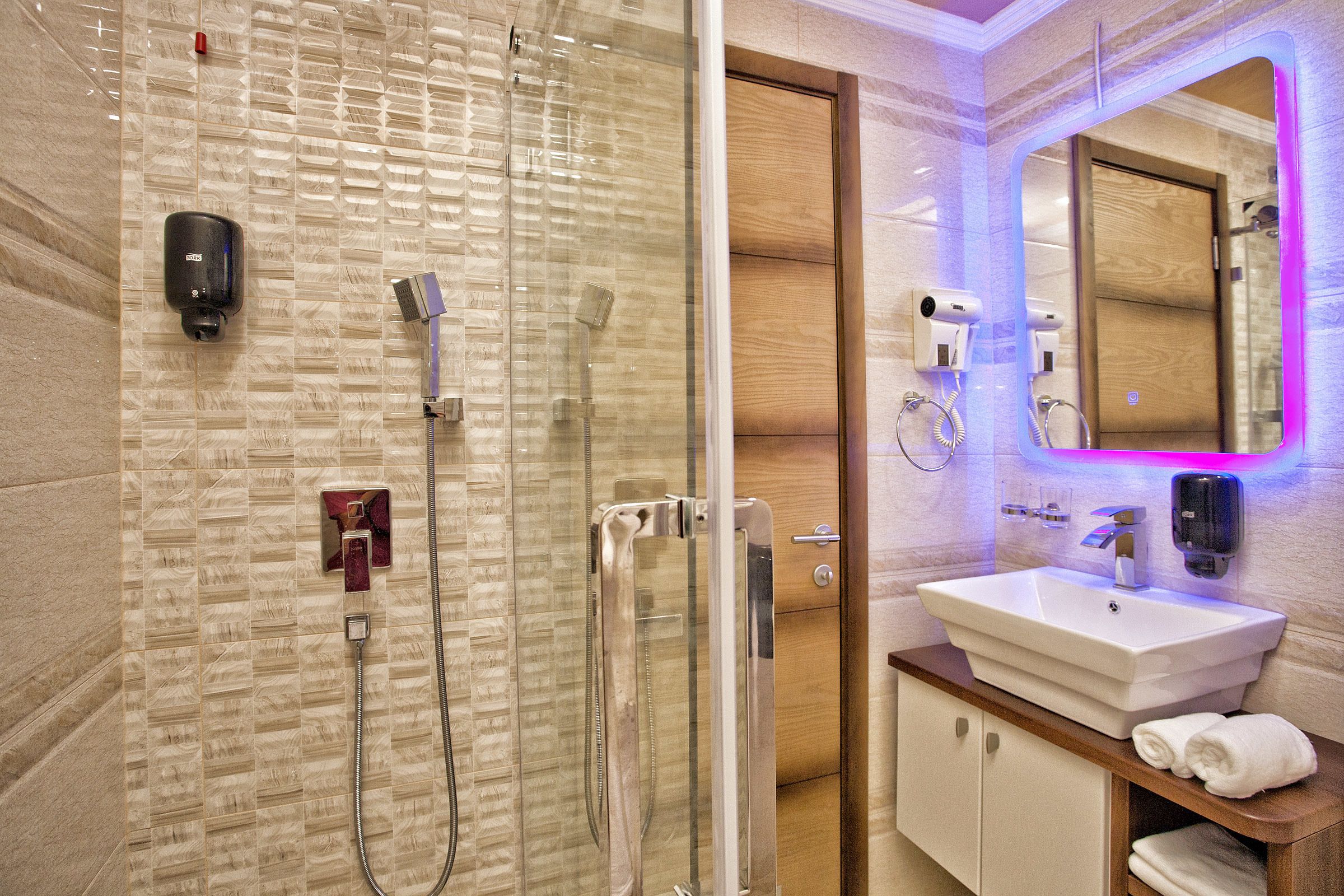 A modern bathroom with a glass-enclosed shower, a white sink, and a wooden vanity.