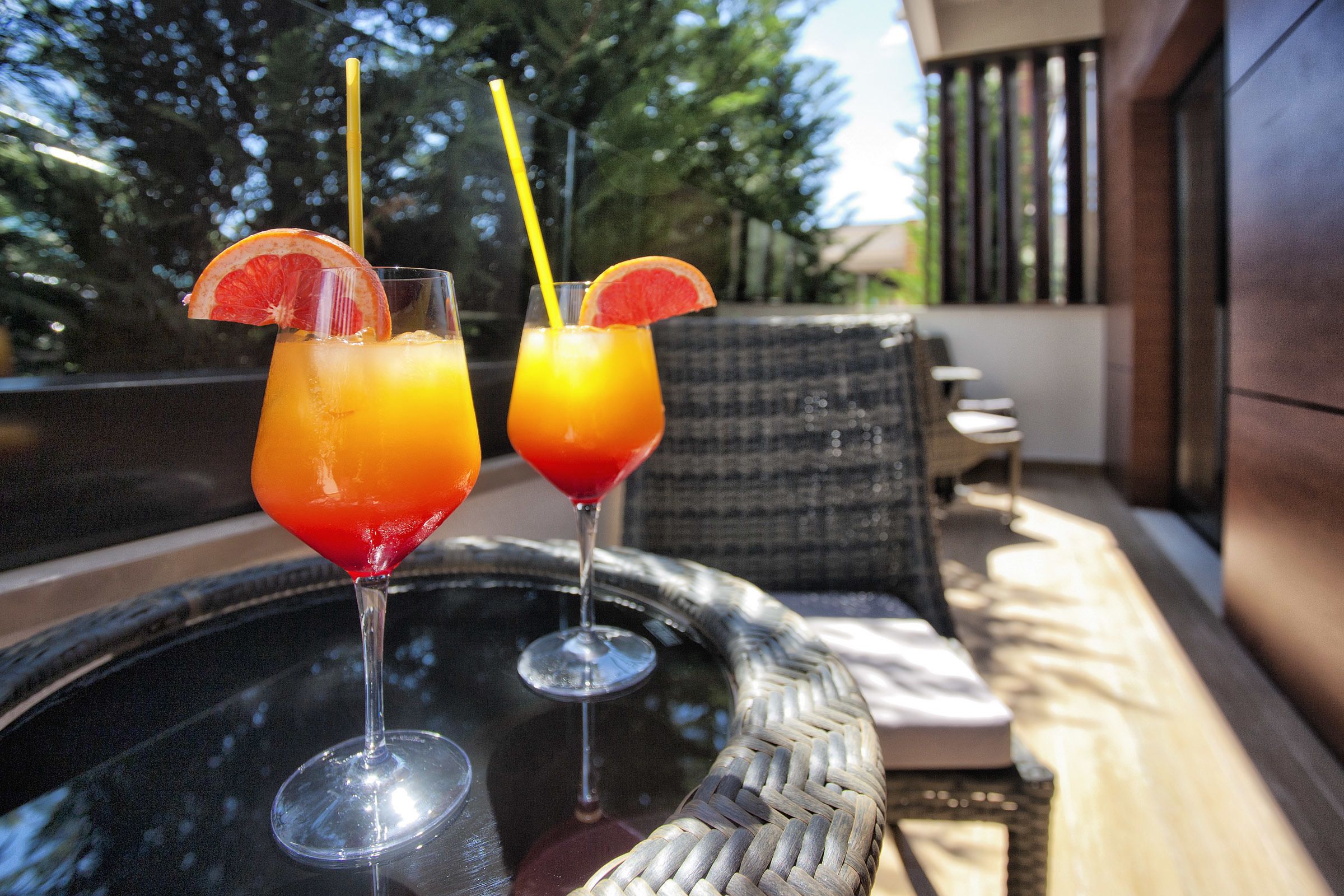 Two drinks on a glass table with a wicker chair in the background.