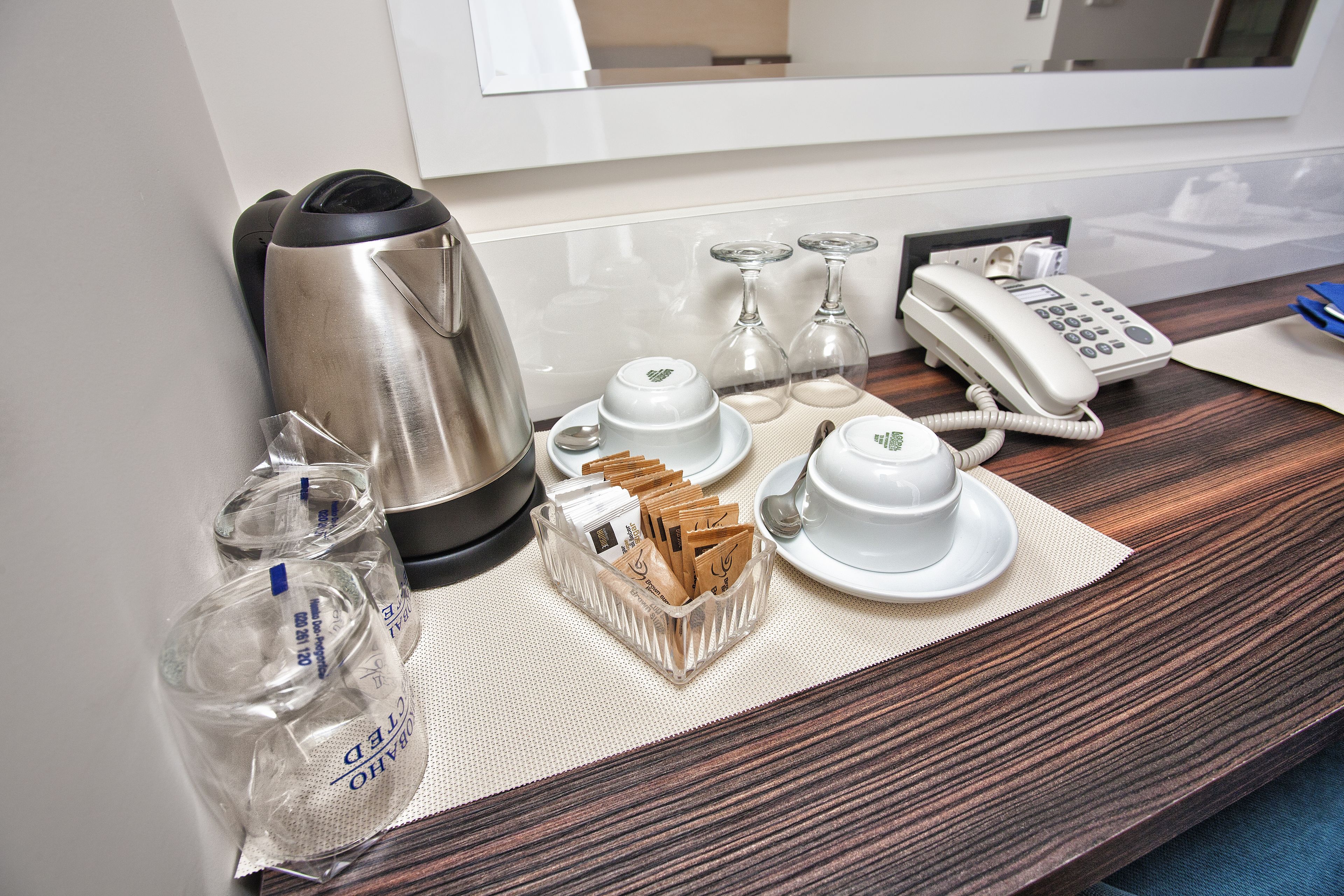A hotel room's breakfast setup with a coffee maker, teapot, cups, and a phone on the counter.