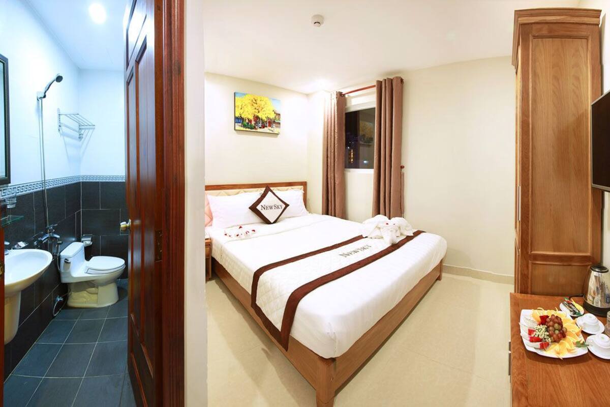 A hotel room with a bed, a TV, a desk with a plate of food, and a bathroom with a sink and toilet.