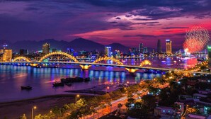 A brightly lit bridge over a river with city buildings in the background. - New Sky Hotel (Da Nang)