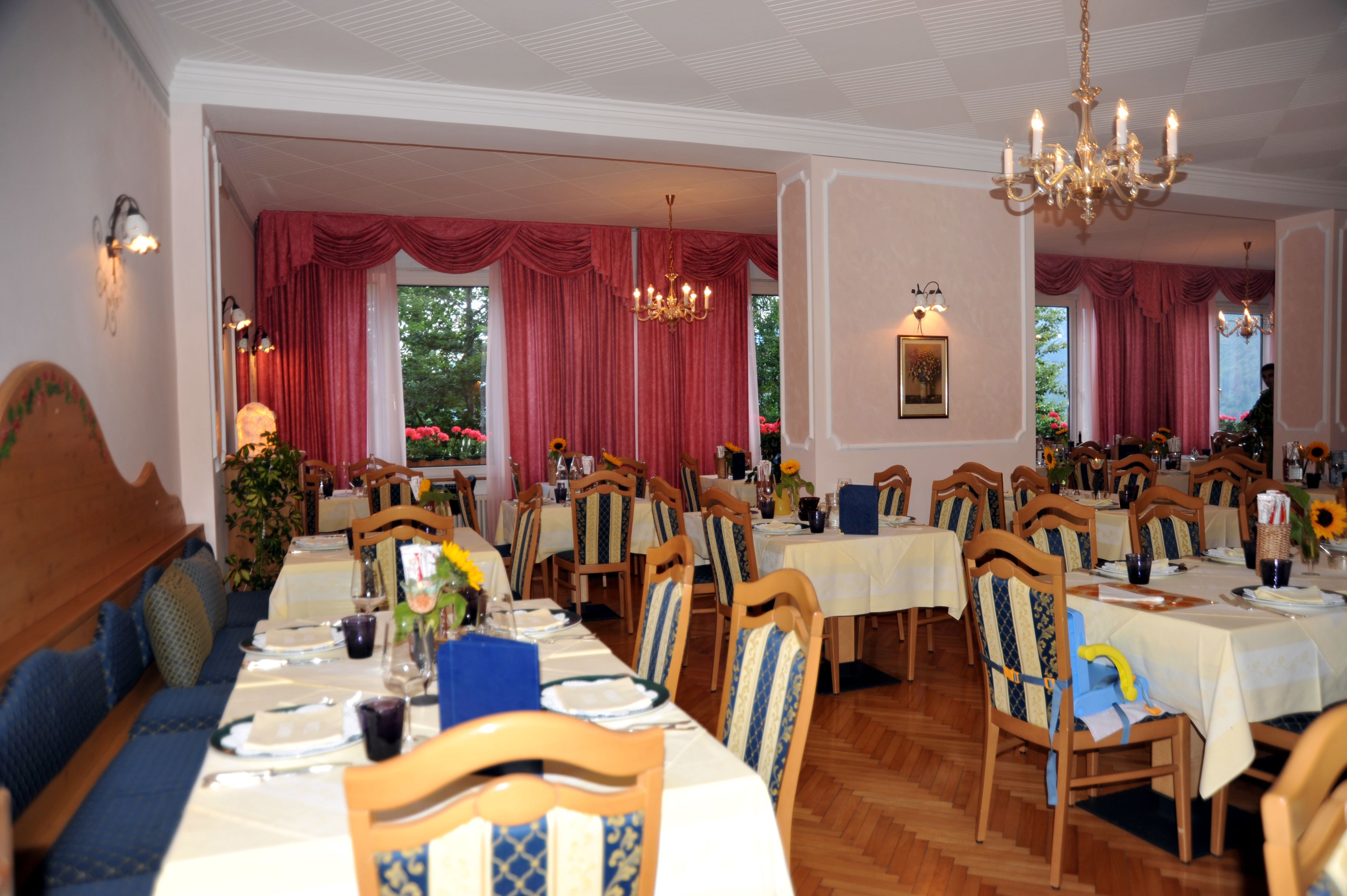 A dining area with multiple tables and chairs, red curtains, and chandeliers.