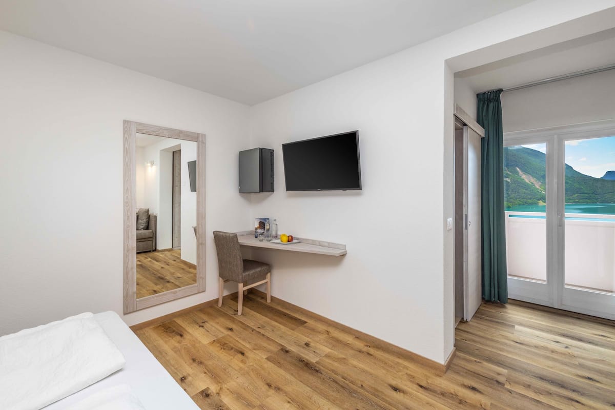 A hotel room with a bed, a desk with a chair, a flat-screen TV, and a large mirror.
