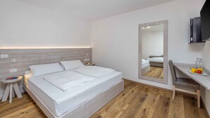 A modern hotel room with a large bed, a bedside table, a mirror, a desk with a chair, and a flat-screen TV. - Hotel Londra (Molveno)