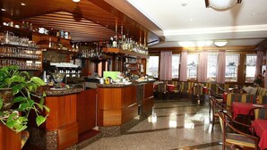 A bar area with wooden shelves, a counter, and seating with tables and chairs. - Hotel Londra (Molveno)