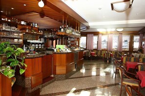 A bar area with wooden shelves, a counter, and seating with tables and chairs. - Hotel Londra (Molveno)