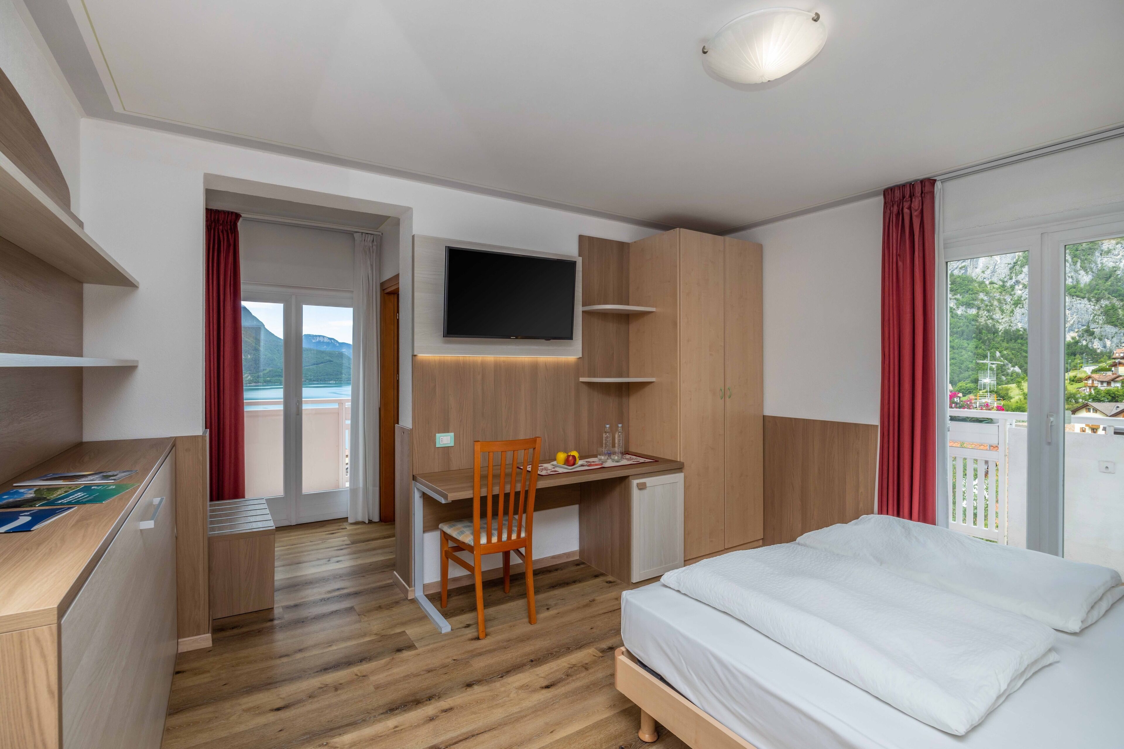 A modern hotel room with a wooden desk, a bed, and a TV mounted on the wall.