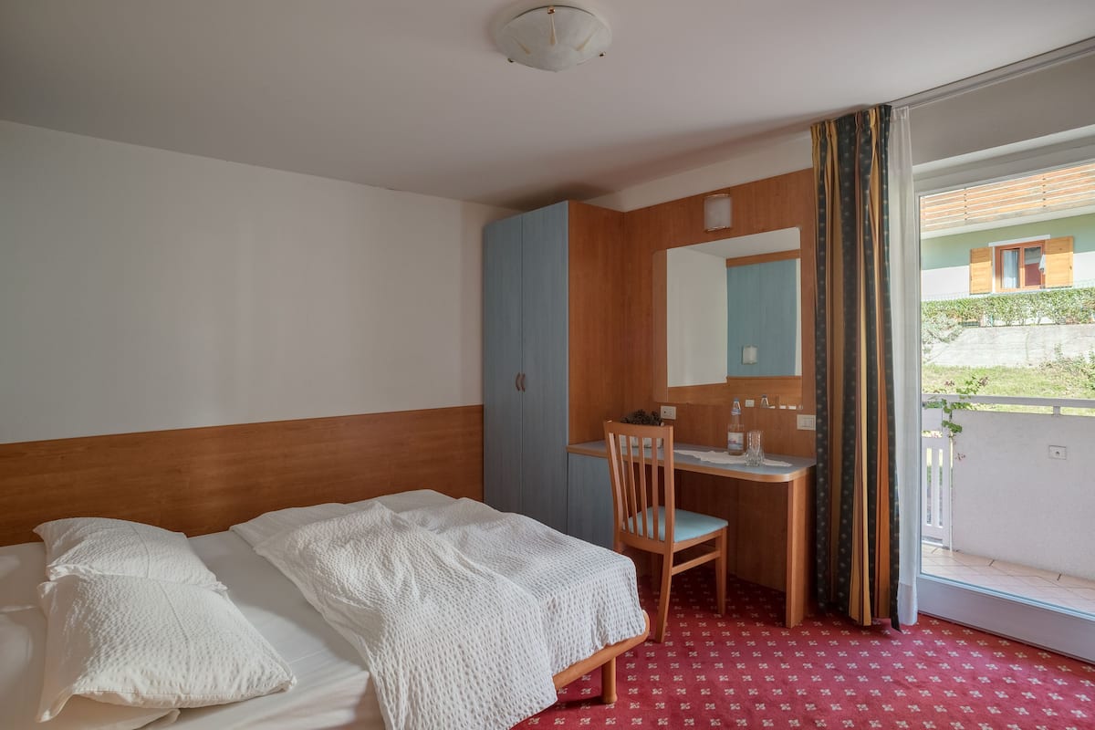 A hotel room with a bed, a desk, a chair, a mirror, and a window with curtains.