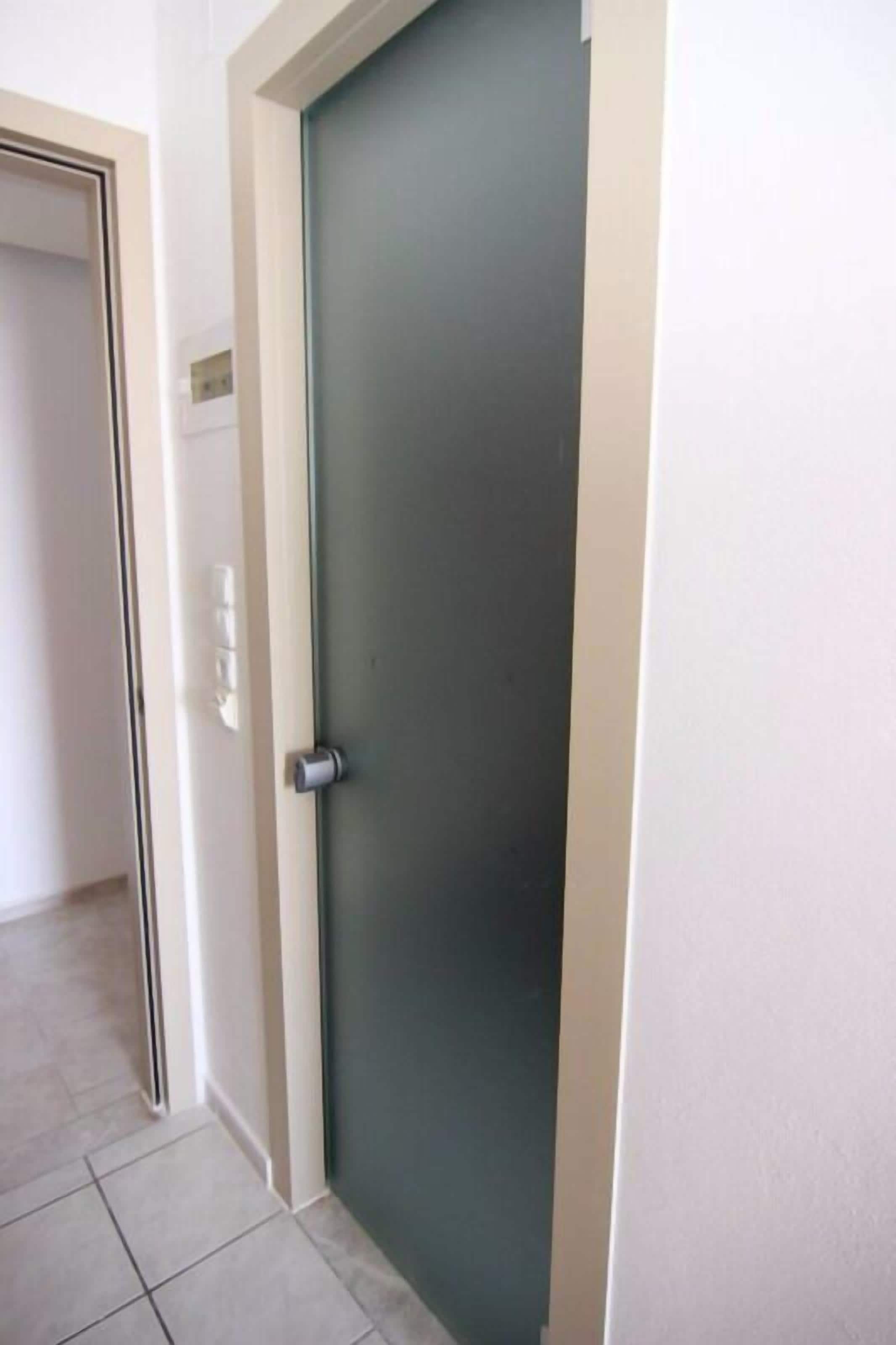 A closed door with a metallic handle and a glass panel, leading to a tiled hallway.