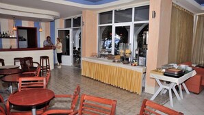 A restaurant with a bar area, wooden chairs, and a counter with food items. - Creta Mare (Agios Vasileios)