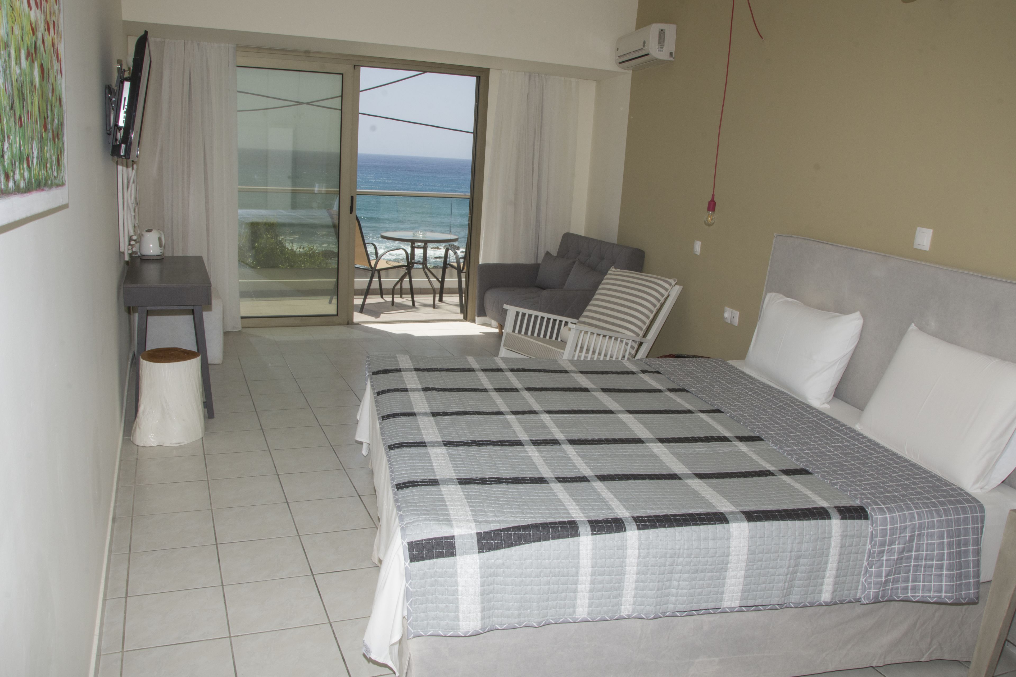 Habitación de hotel con cama, escritorio, silla y vista al océano a través de una puerta corrediza.