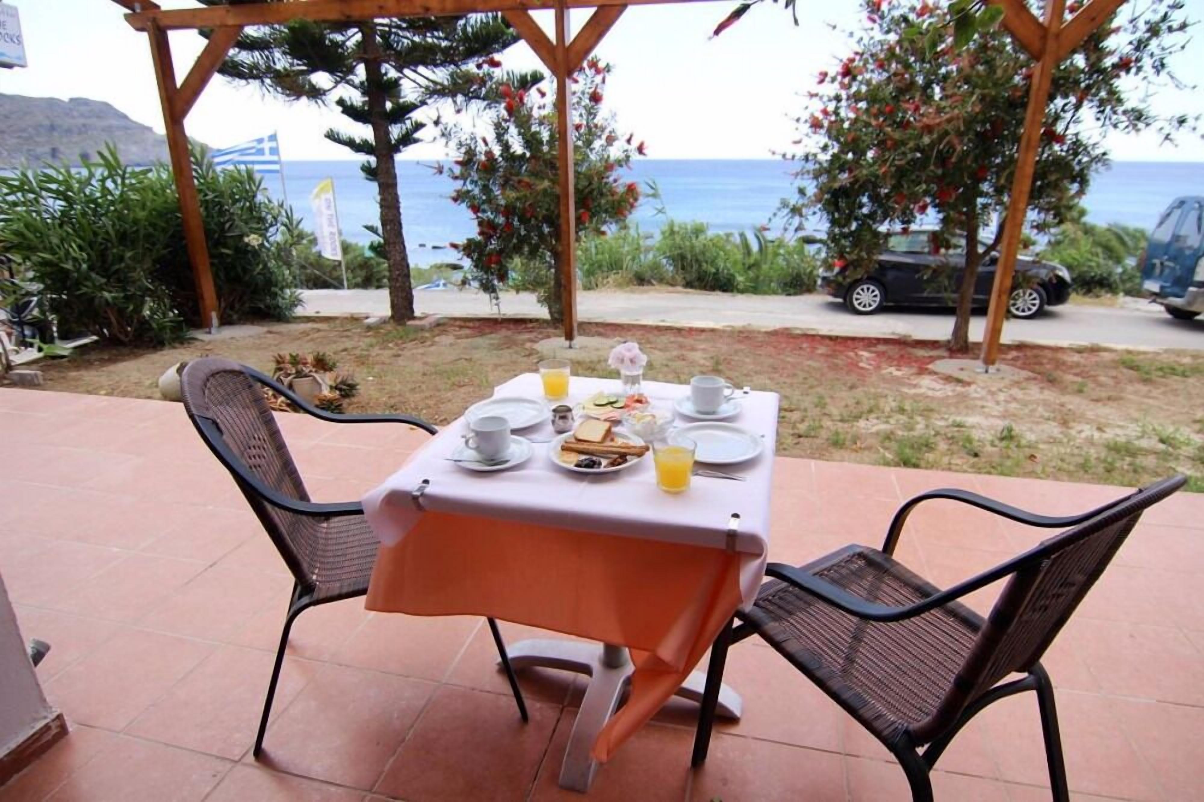 A table set for breakfast with a view of the sea, two chairs, and a pergola structure.