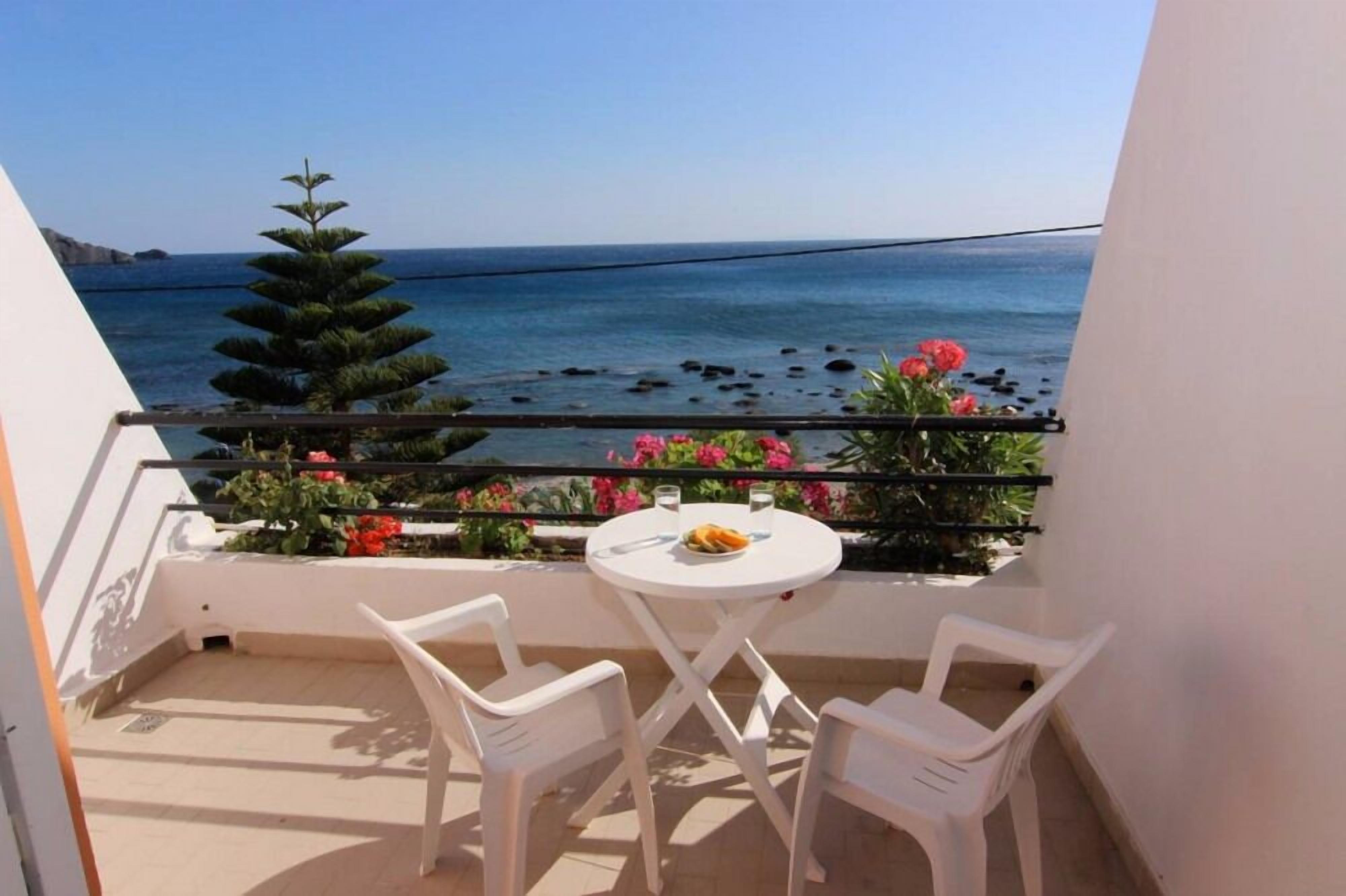 A balcony with a table and chairs, overlooking the sea with a railing and potted plants.