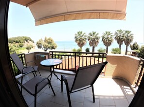 Un balcón con mesa y sillas, con vista a una playa y palmeras.