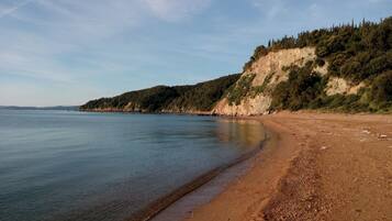 A beach with a clear view of the sea and a rocky cliff with sparse vegetation.