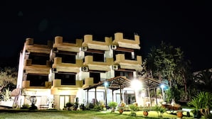 Un hôtel à plusieurs étages doté de balcons, de climatiseurs et d’un espace extérieur bien éclairé, agrémenté de plantes et d’un coin salon abrité.