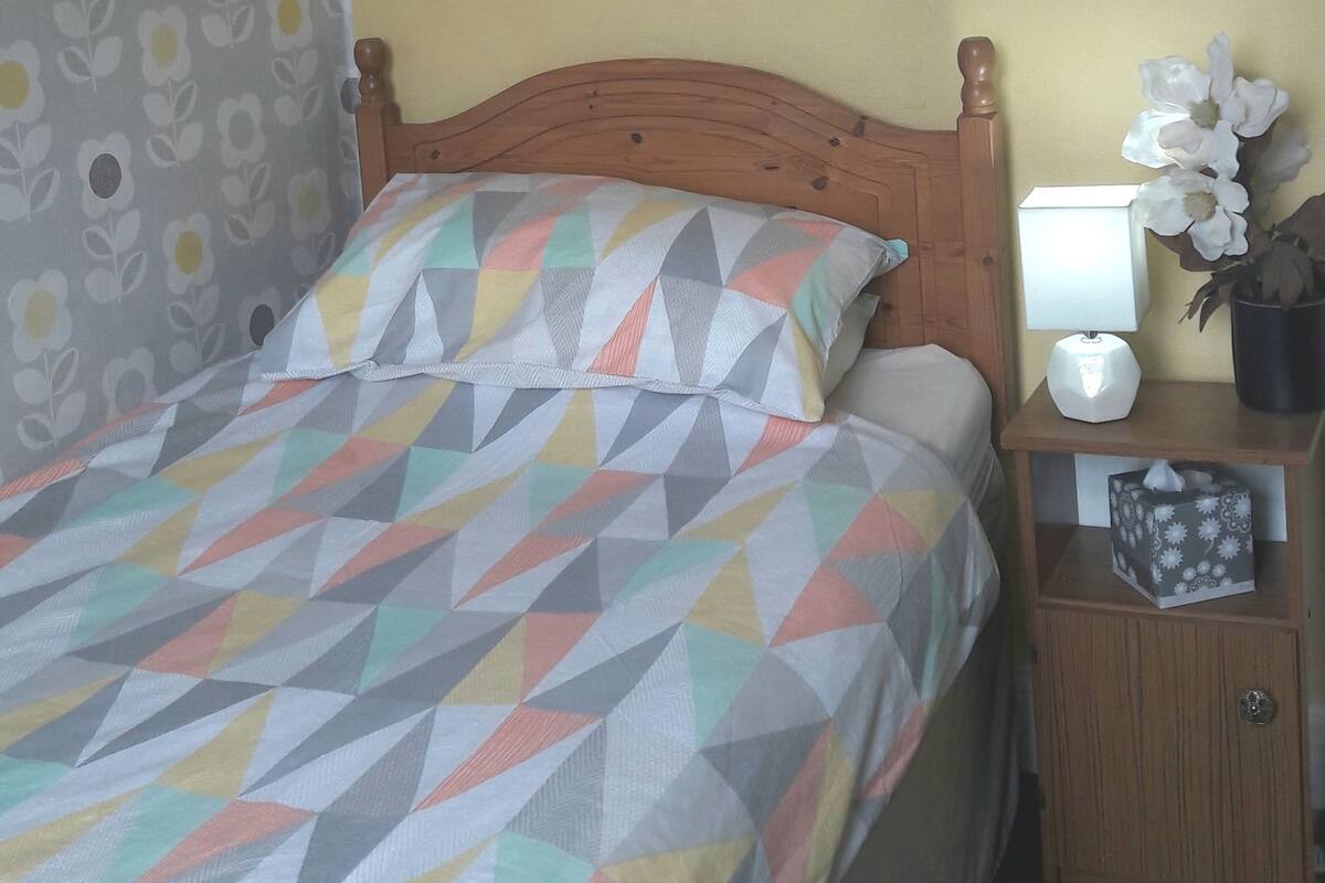 A bedroom with a bed, a nightstand, a lamp, and a wall decoration.