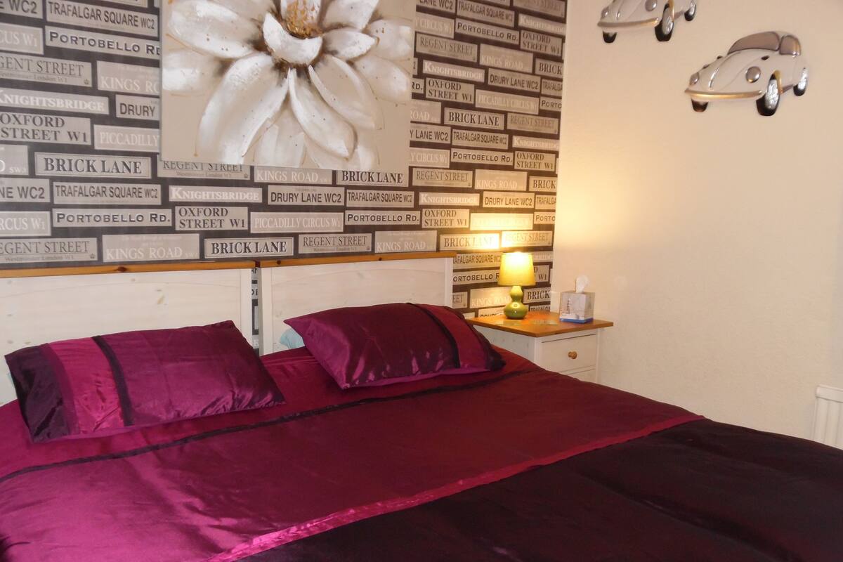 A bedroom with a bed, pillows, a nightstand, a lamp, and a wall with street name signs.