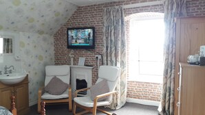 A bathroom with a white sink, mirror, and two chairs with cushions. A television is mounted on the brick wall above the fireplace. - Kirk Lea Guest House (Halifax)