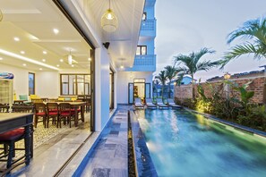 A modern hotel interior with a dining area, a pool, and a staircase leading to the upper floors.