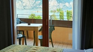 A room with a bed, a table, and chairs, overlooking a scenic view of mountains and a body of water. - Villa Isabella Hotel & Residence (Brenzone sul Garda)