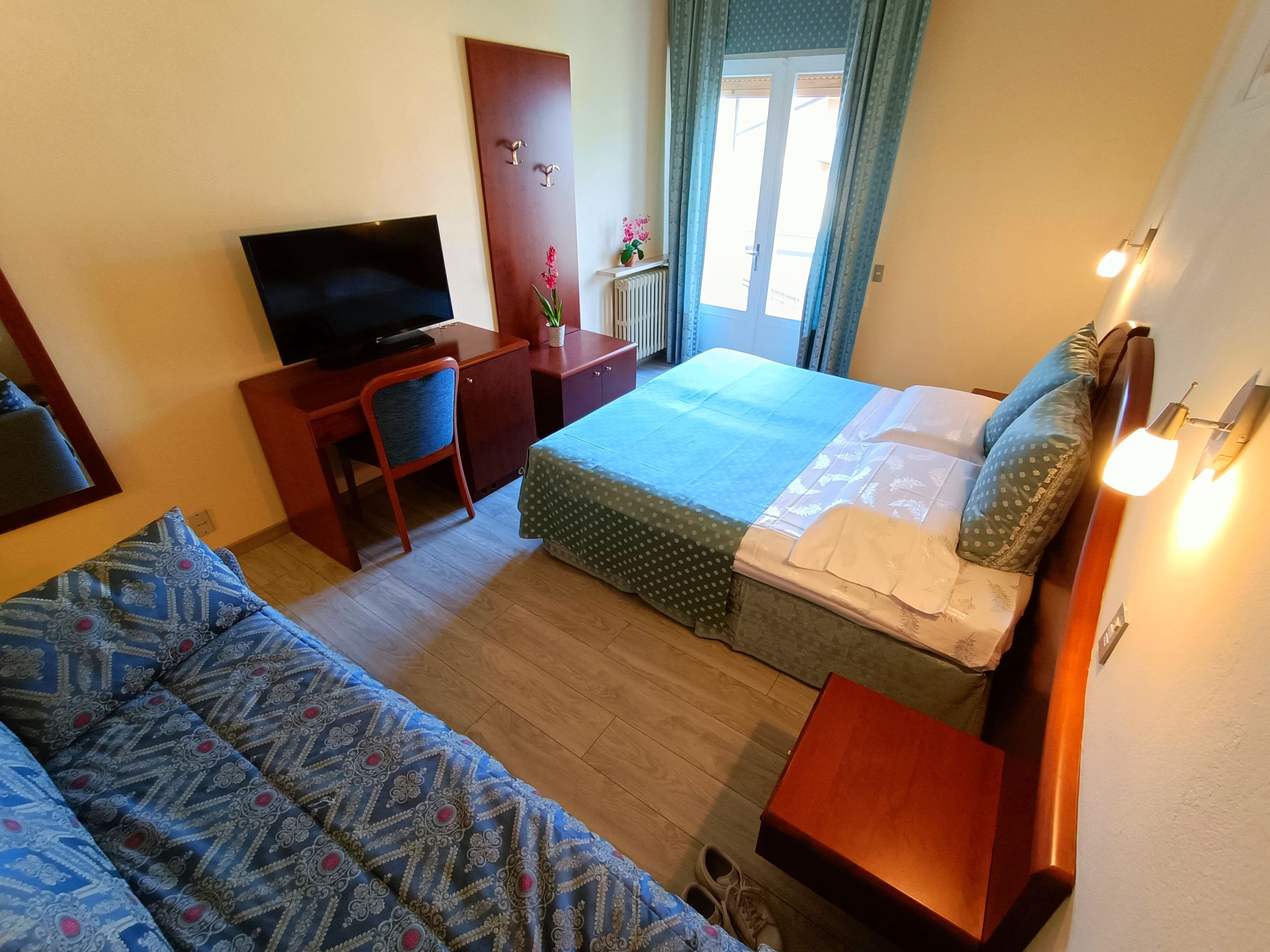 Een hotelkamer met een bed, een bureau met een televisie, een stoel, een klein tafeltje en een bank.