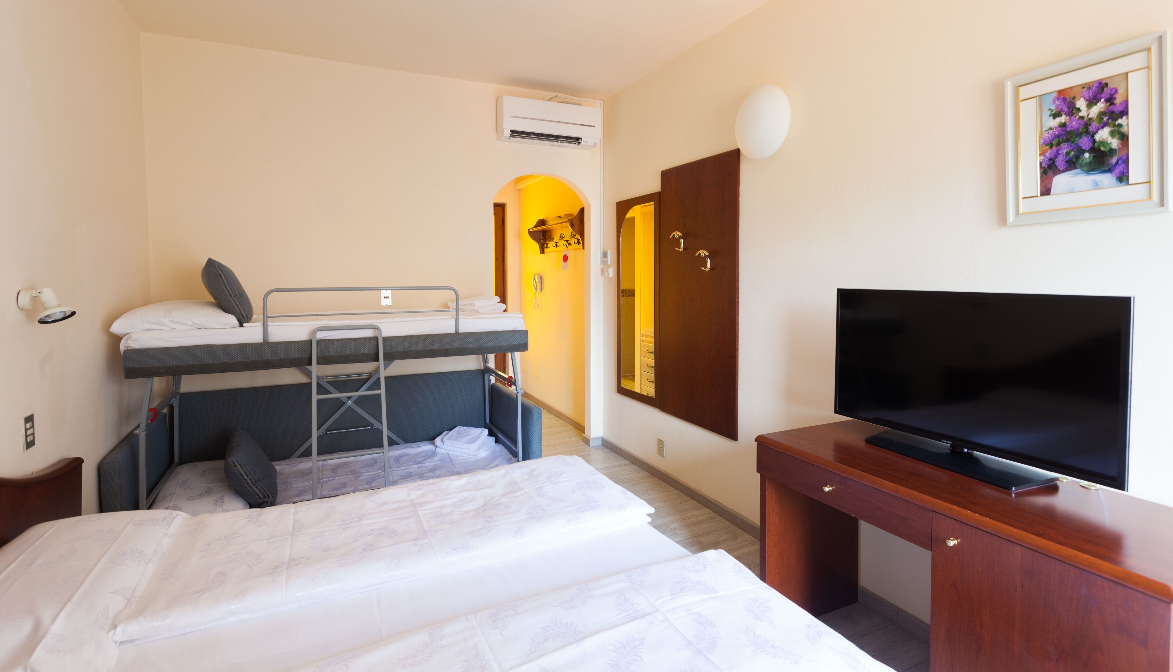 Ein Hotelzimmer mit Etagenbett, Schreibtisch, Flachbildfernseher, Holzkommode und einem gerahmten Bild an der Wand.