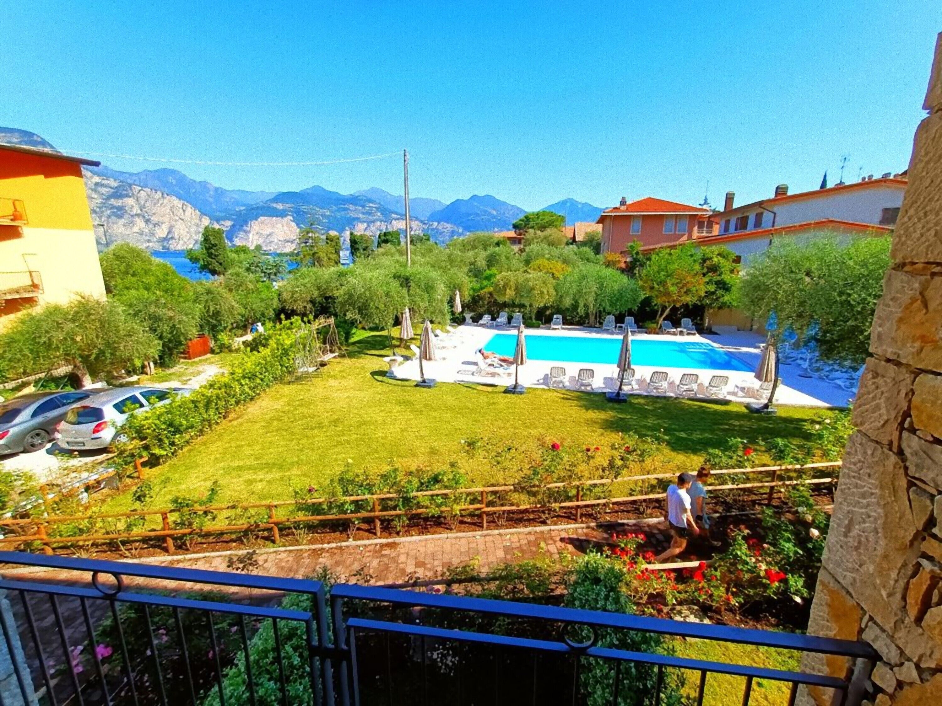 A residential area with a swimming pool surrounded by greenery, a view of mountains, and a clear sky.