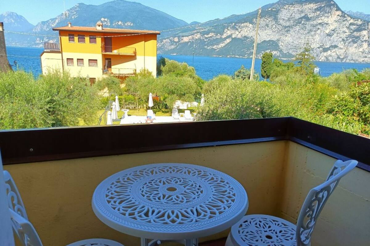 Een balkon met twee witte stoelen en een tafel, met uitzicht op een bergachtig landschap en een wateroppervlak.