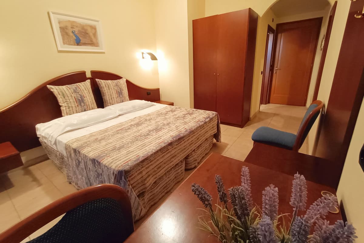 Een hotelkamer met een bed, een bureau, een stoel, een kledingkast en een schilderij aan de muur.