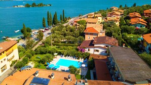 A coastal town with a swimming pool surrounded by villas, a marina, and mountains in the background. - Villa Isabella Hotel & Residence (Brenzone sul Garda)