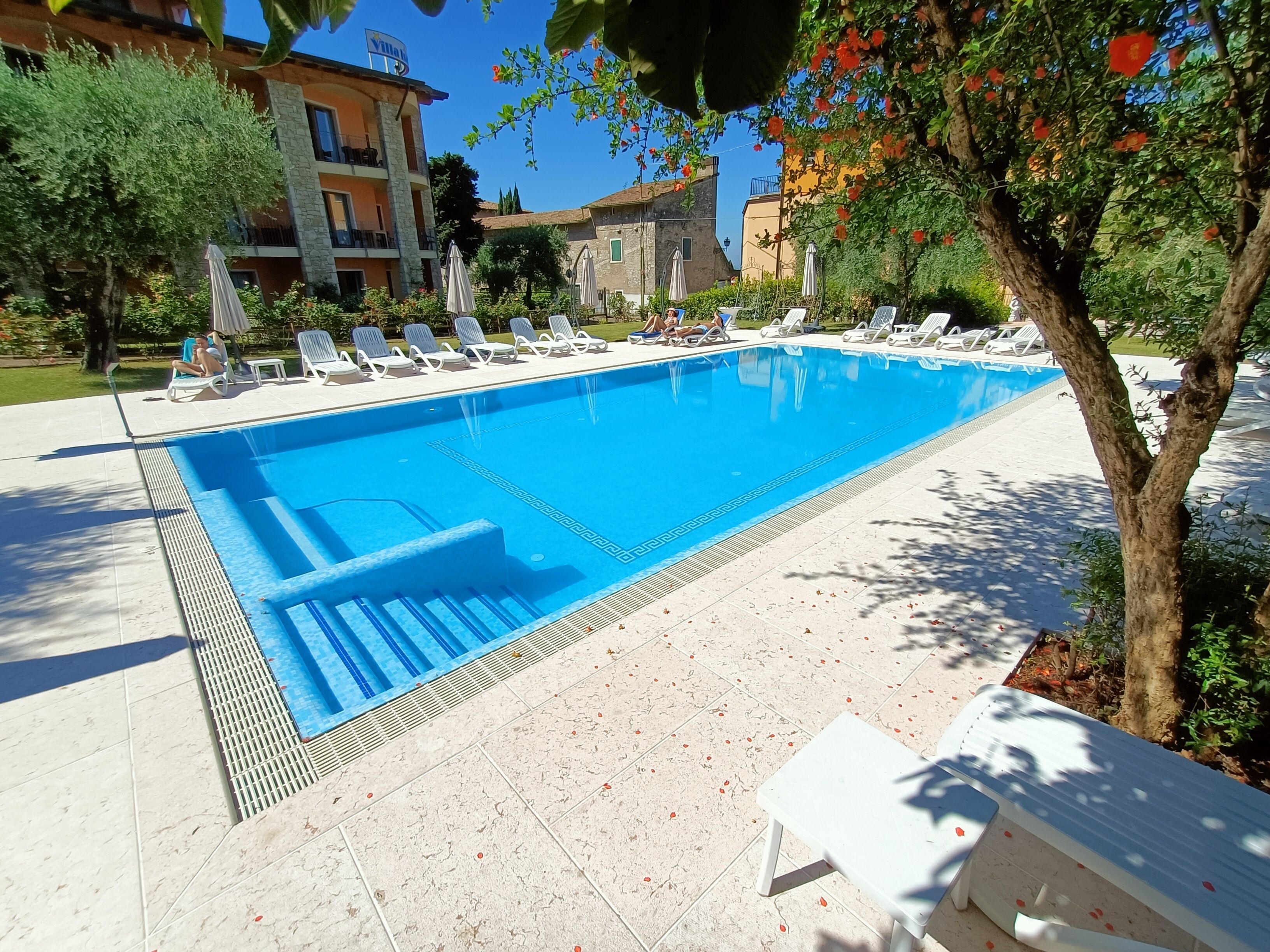 A swimming pool with lounge chairs and a small table, surrounded by trees and buildings.
