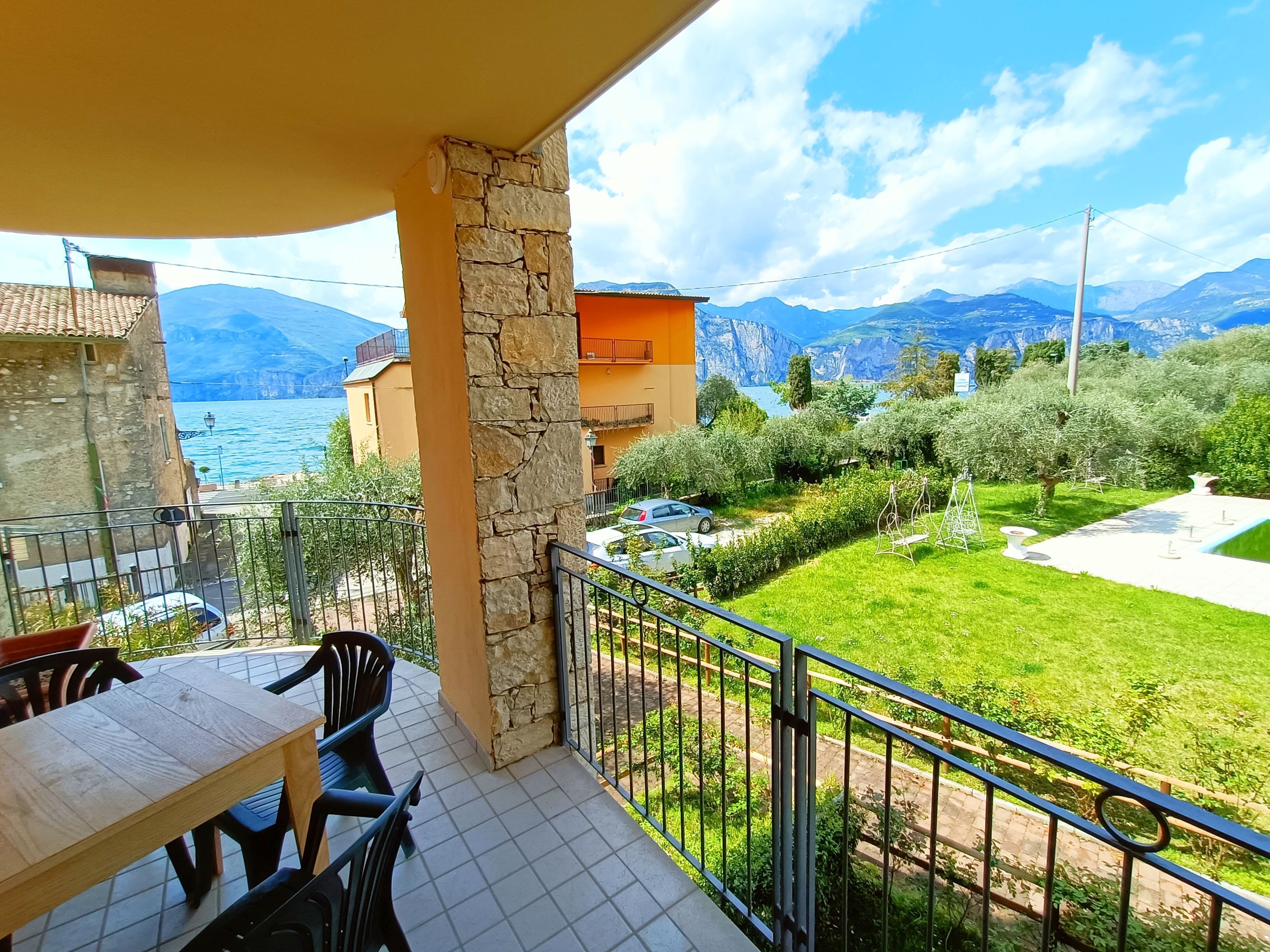 A balcony with a stone pillar, a table with chairs, and a view of a lake and mountains.