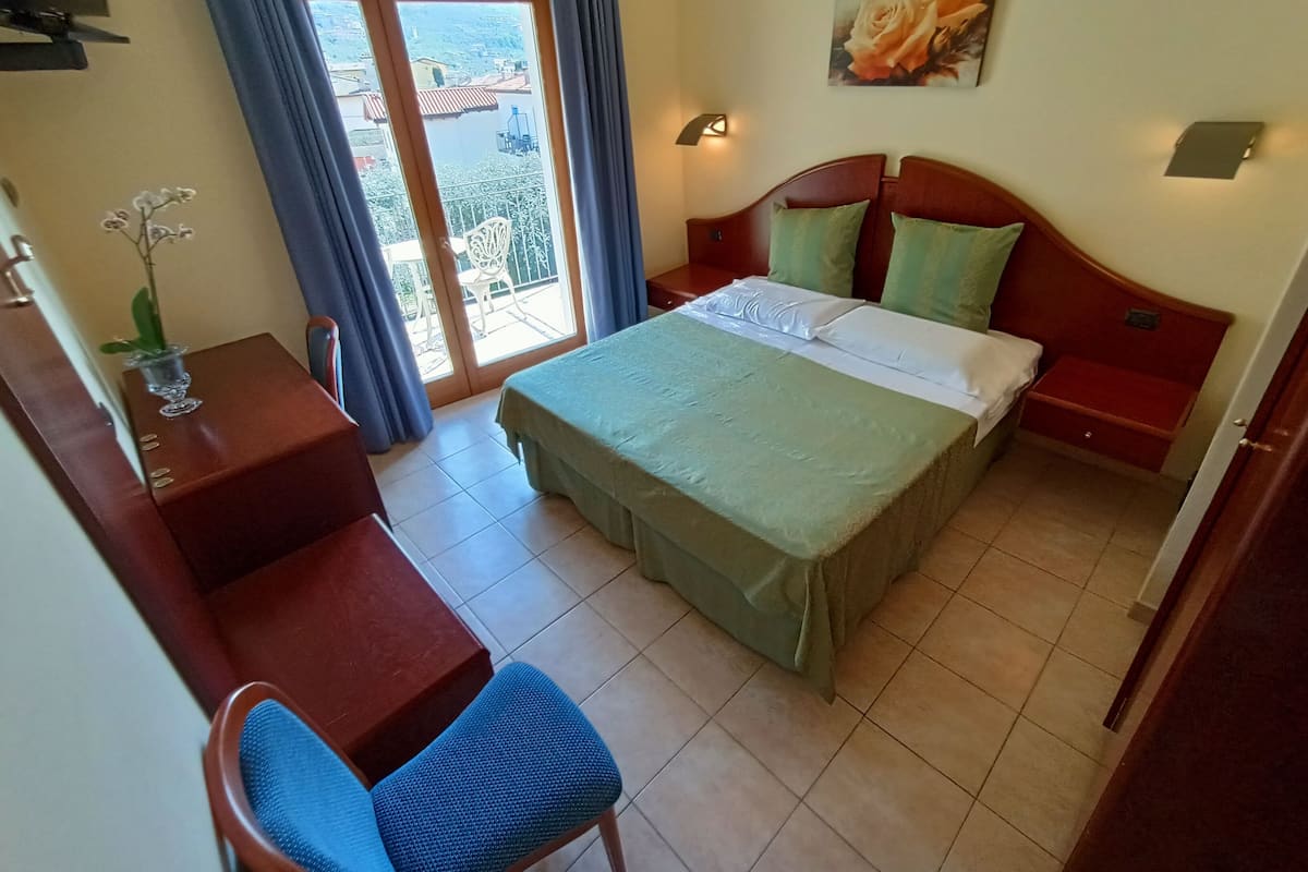 Een hotelkamer met een bed, een bureau, een stoel, een klein tafeltje met een vaas en uitzicht buiten door een schuifdeur.