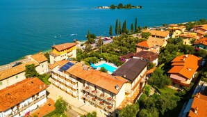 A coastal town with a prominent hotel featuring balconies, a swimming pool, and a view of the lake and mountains. - Villa Isabella Hotel & Residence (Brenzone sul Garda)