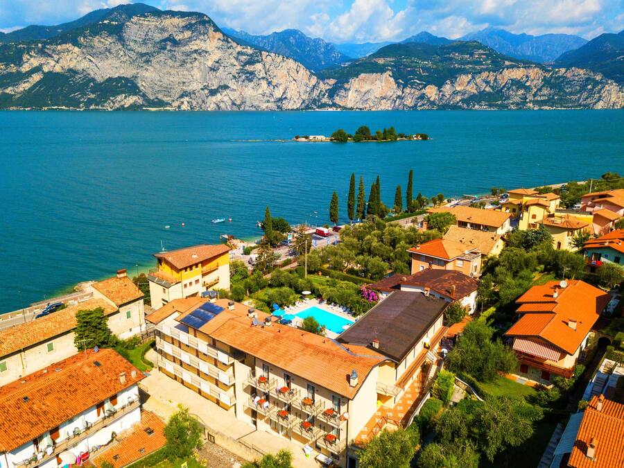 Un pueblo costero con un hotel destacado que cuenta con balcones, una piscina y vistas al lago y a las montañas.