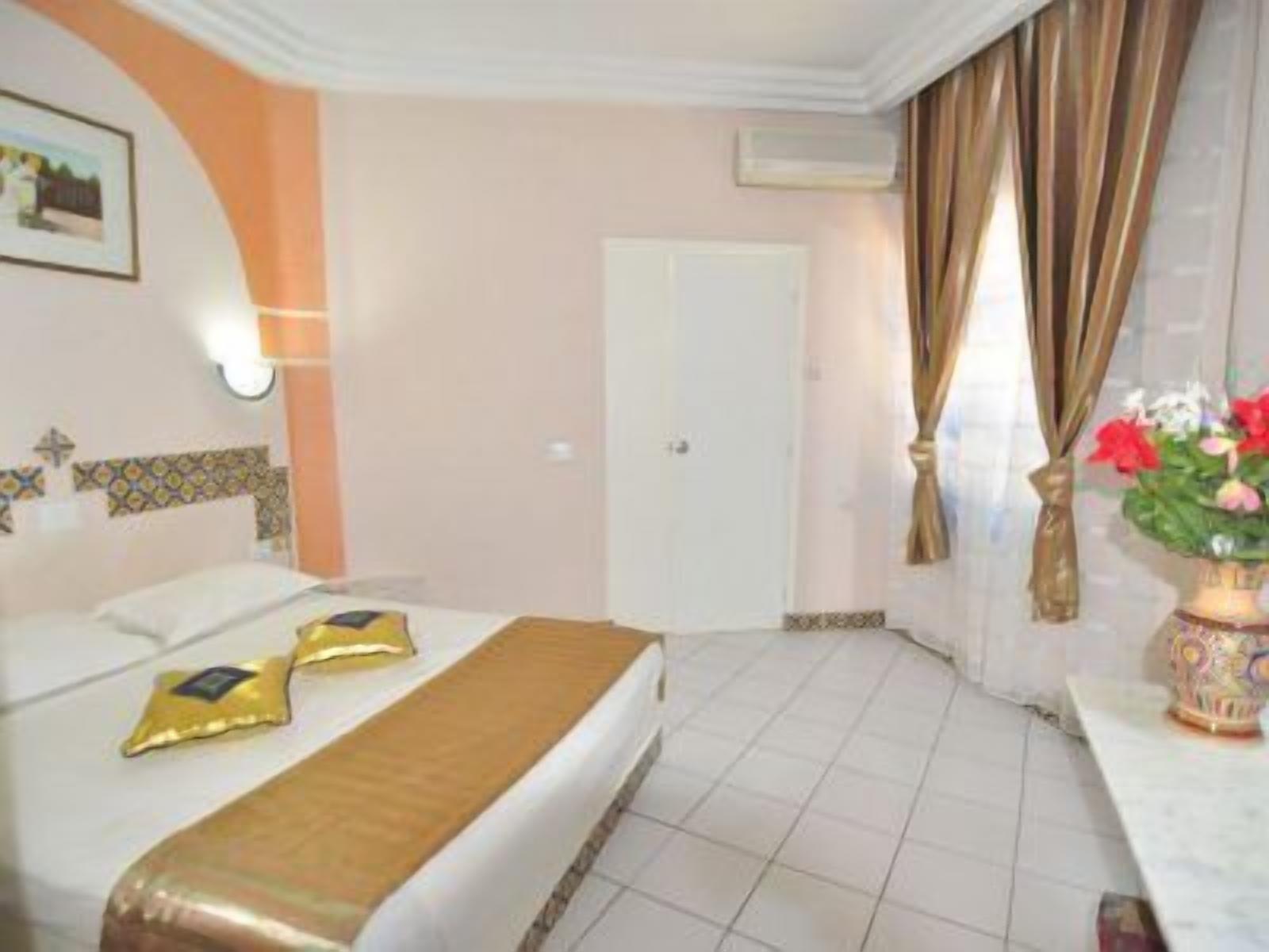 Une chambre d’hôtel avec un lit, une table de chevet, un vase avec des fleurs et une porte.
