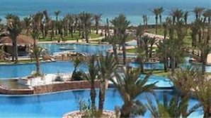 A resort with multiple swimming pools surrounded by palm trees and a view of the ocean.