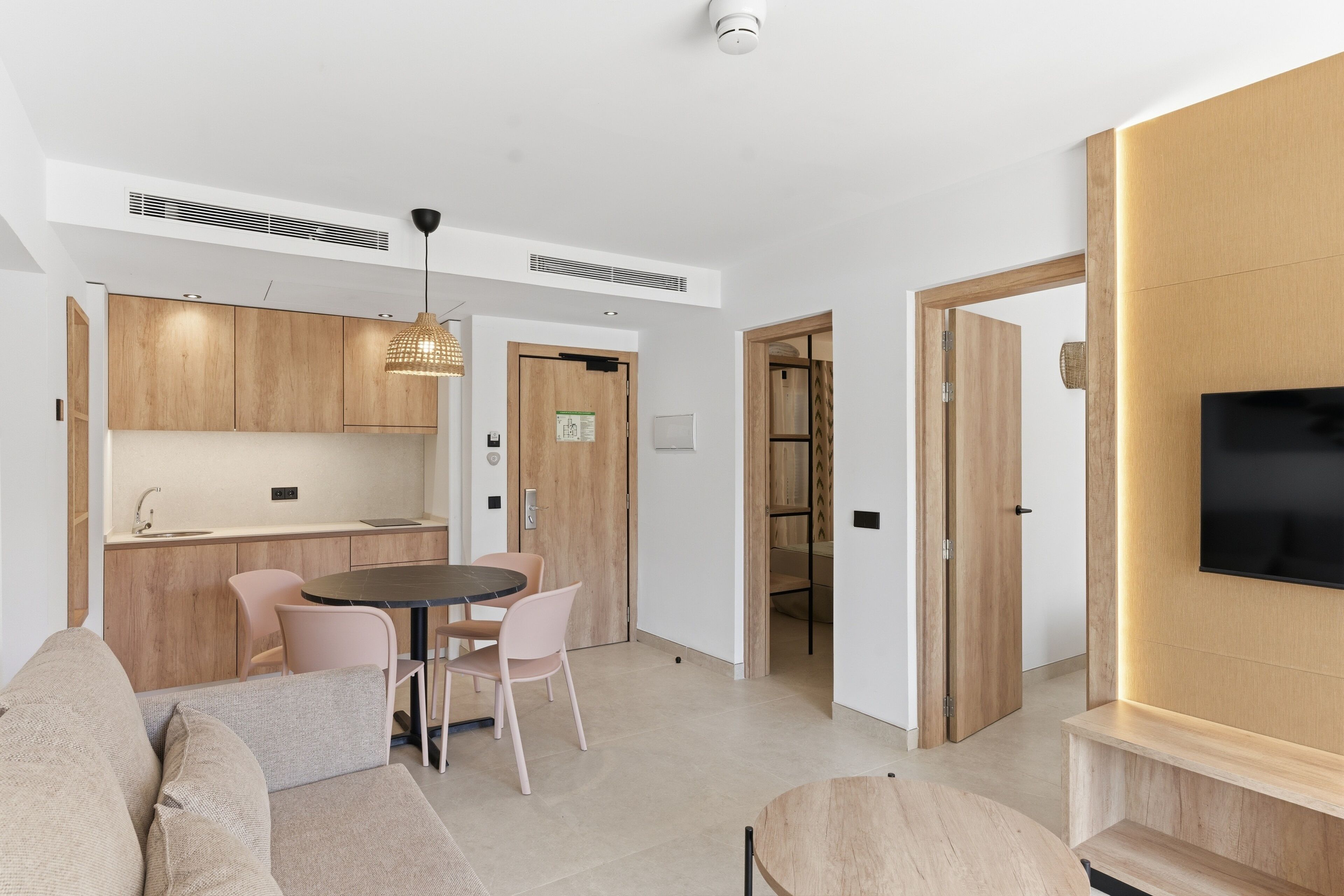 Een moderne woonkamer met een bank, een eettafel met stoelen, een aan de muur bevestigde televisie en een keuken met houten kastjes en een spoelbak.